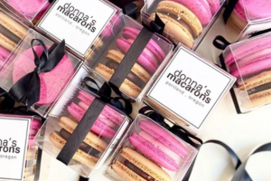 Gift boxes with two French macarons inside, one pibk and one brown with dark filling.